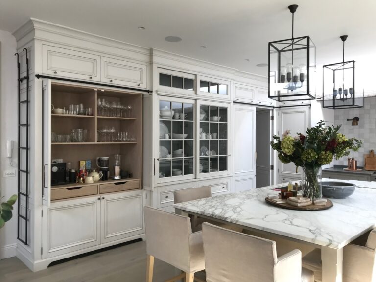 Kitchen with white painted cabinetry, glazed display dresser, stone-topped island and lantern pendant lights above