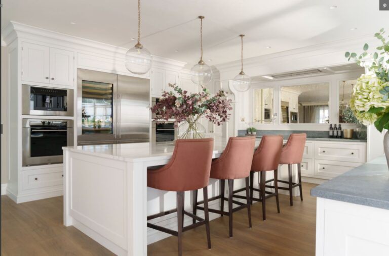 White painted kitchen with large island, terracotta bar stools, integrated fridge and glass pendant lighting above