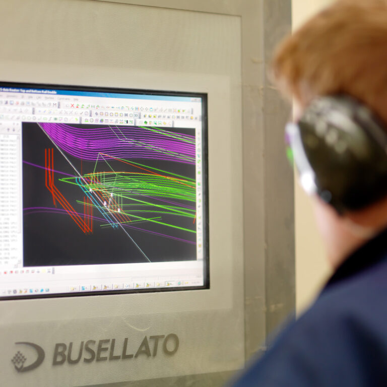 Workshop screen showing CAD cutting diagrams for a joinery component, viewed by someone wearing ear defenders nearby