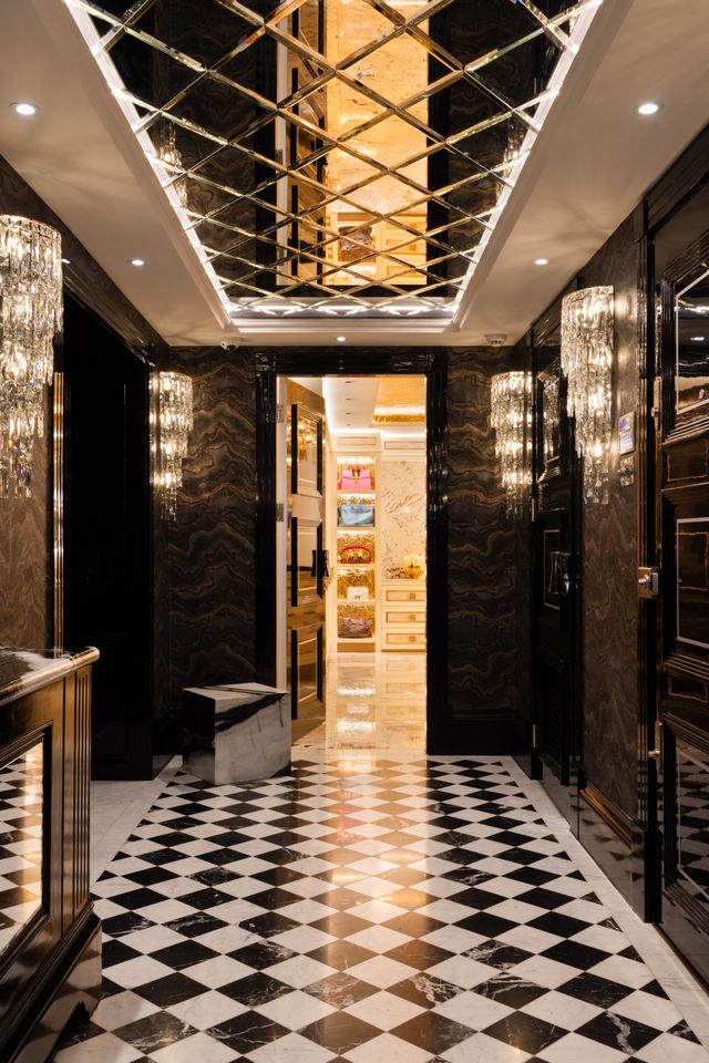 A mirrored hallway with chequered stone flooring, crystal wall lights, and glimpses into an illuminated dressing room beyond