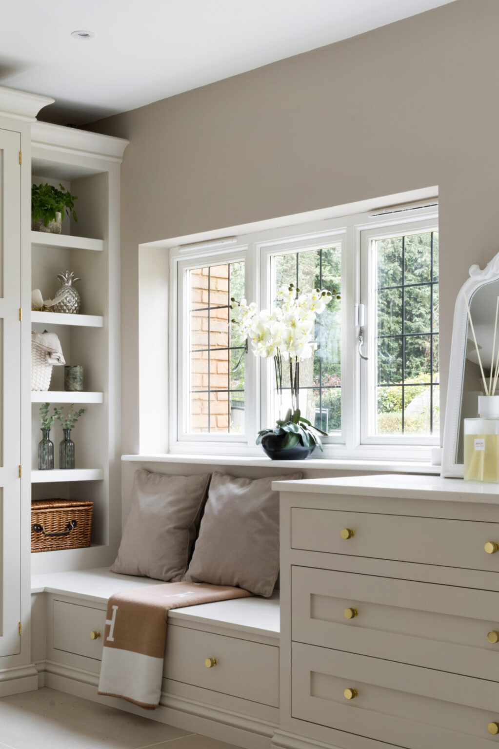 Boot room window seat with cushions and drawers beneath, flanked by open shelving and brushed gold hardware