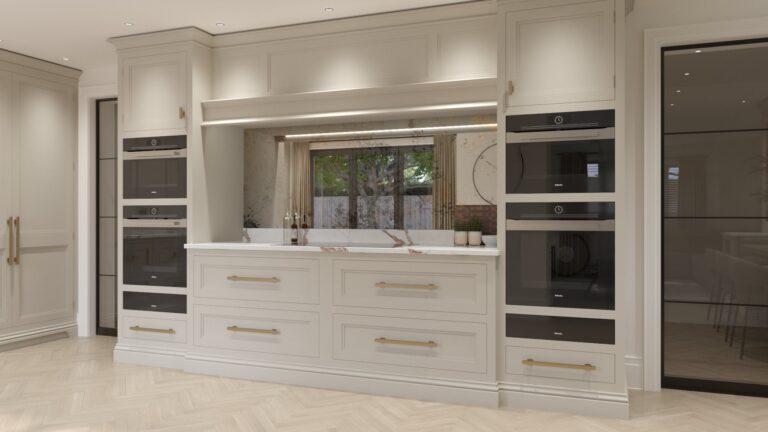 Kitchen wall of cream cabinetry with integrated ovens, brass handles and a stone-topped worktop beneath a mirrored splashback
