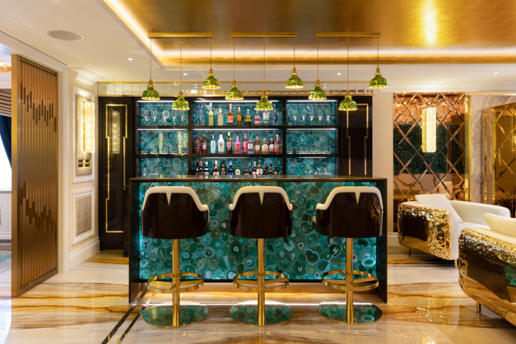 Backlit green agate bar with gold pendant lights, brass-framed stools and a fully stocked drinks display