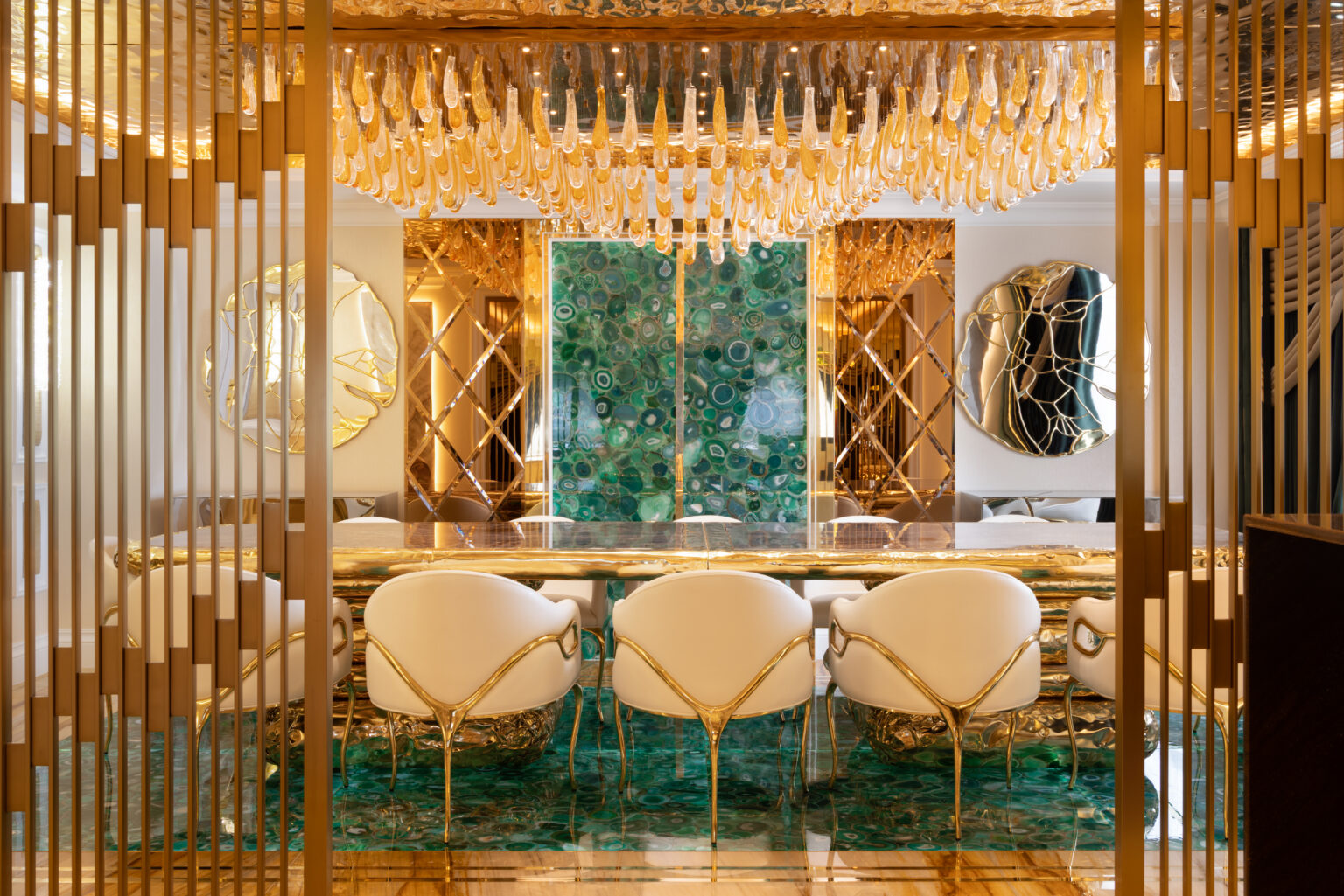 Dining area with a green agate table and panelling, gold-framed chairs, and a hanging gold glass chandelier