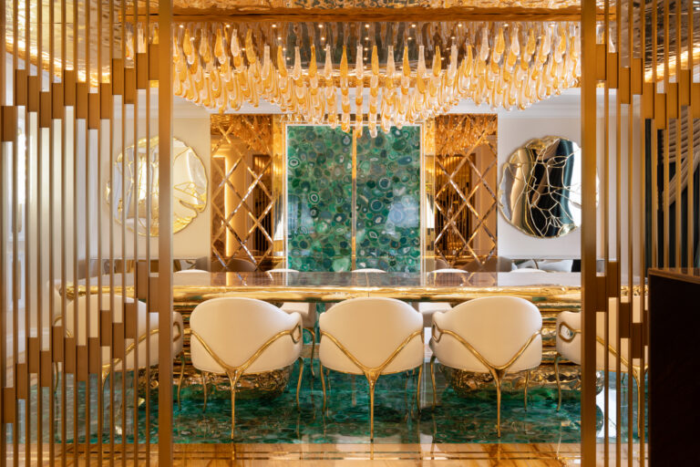 Dining area with a green agate table and panelling, gold-framed chairs, and a hanging gold glass chandelier