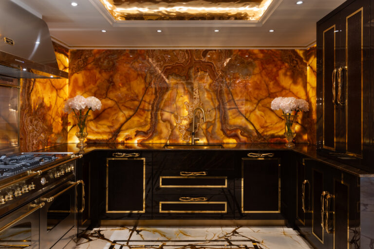 Kitchen with a backlit onyx splashback, chocolate lacquer cabinetry, gold handles and a range cooker beneath an extractor hood