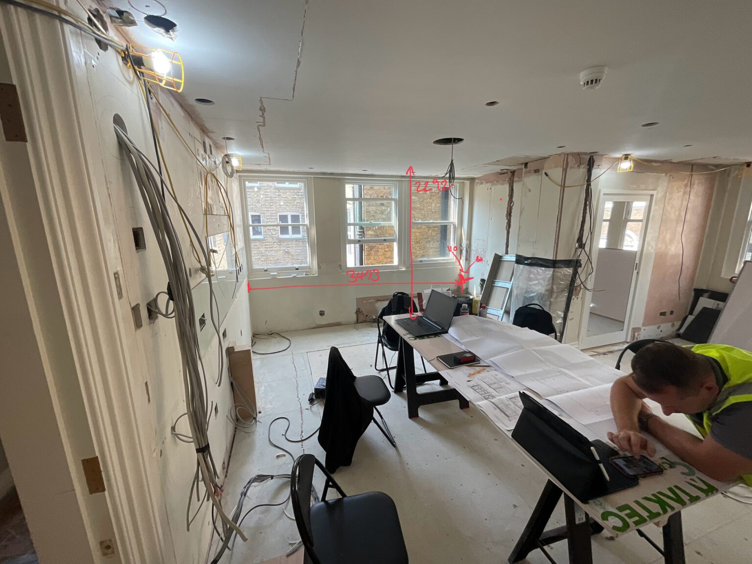 The penthouse kitchen space stripped back to a shell during the build, with exposed services and site drawings on a trestle table