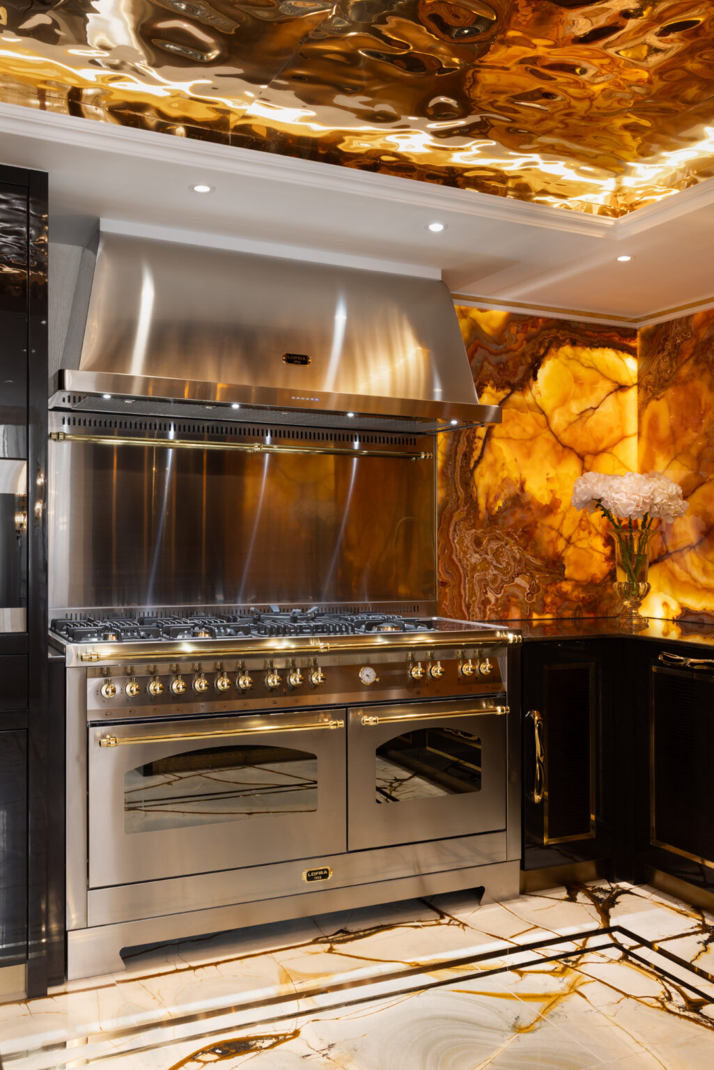 Range cooker with brass trim beneath a backlit onyx splashback and mirrored gold ceiling panel
