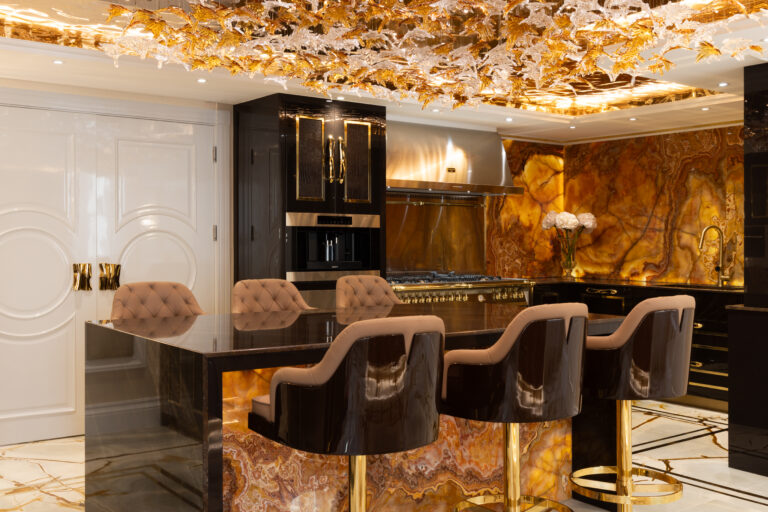 Kitchen island with upholstered bar stools, gold fittings, and a decorative crystal ceiling feature above