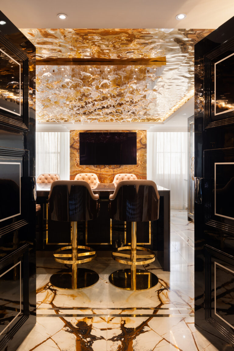 Backlit onyx island and wall panel with gold-framed stools beneath a sculptural glass ceiling feature