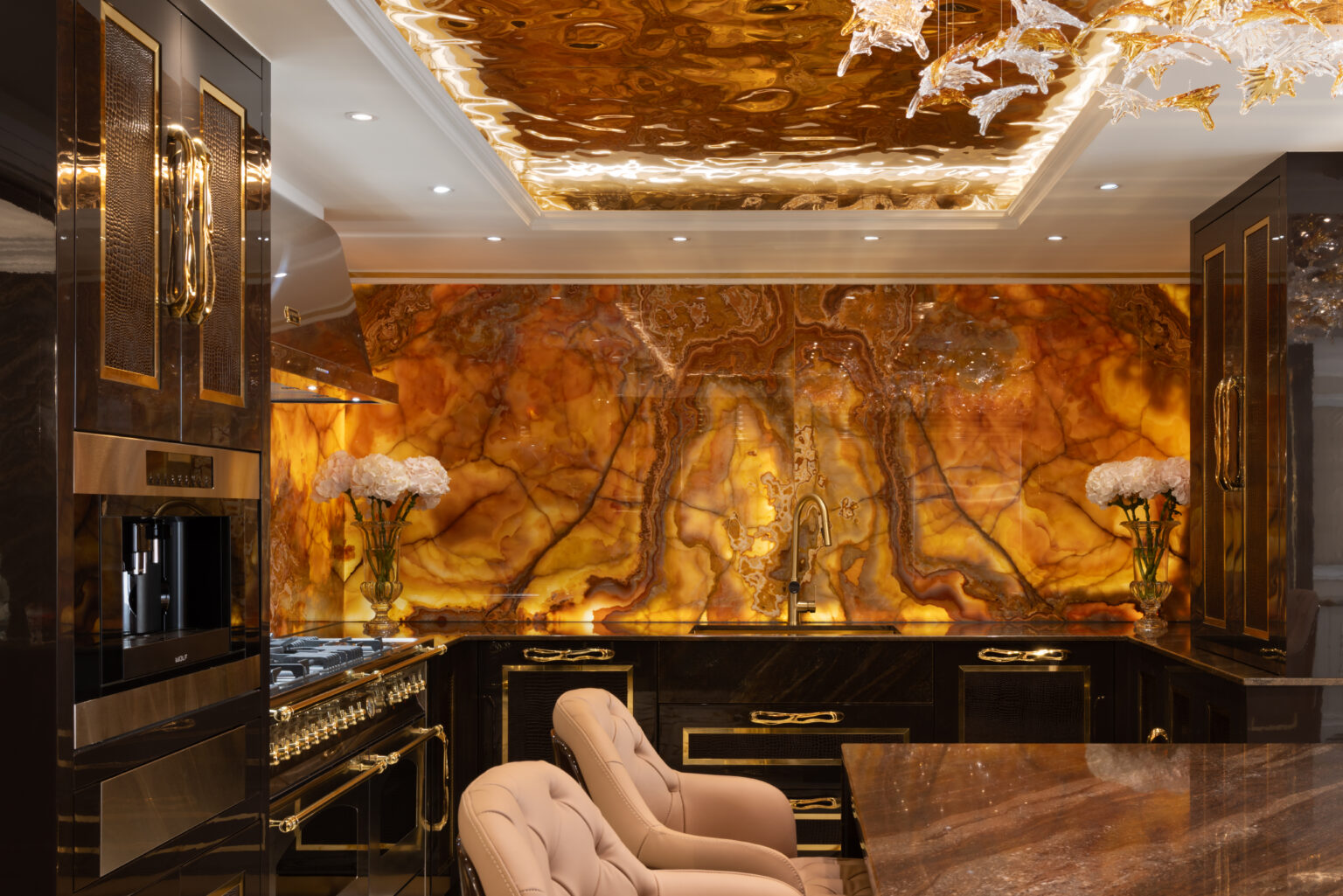 Kitchen with backlit onyx splashback and ceiling panel, gold-trimmed black cabinetry and tufted blush bar stools
