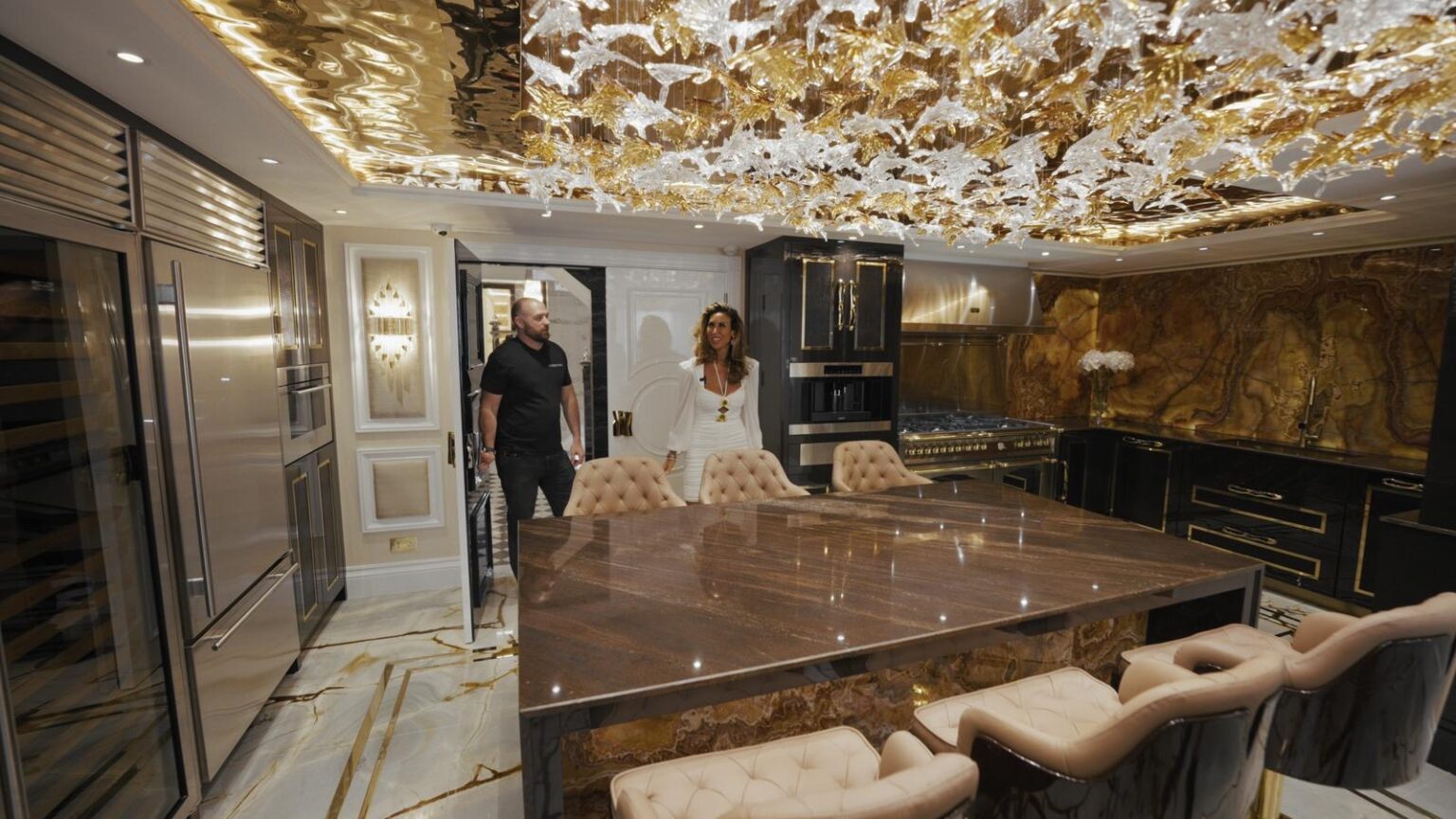 Kitchen island topped in Quicksand Brown granite beneath a backlit onyx wall and ornate gold ceiling feature