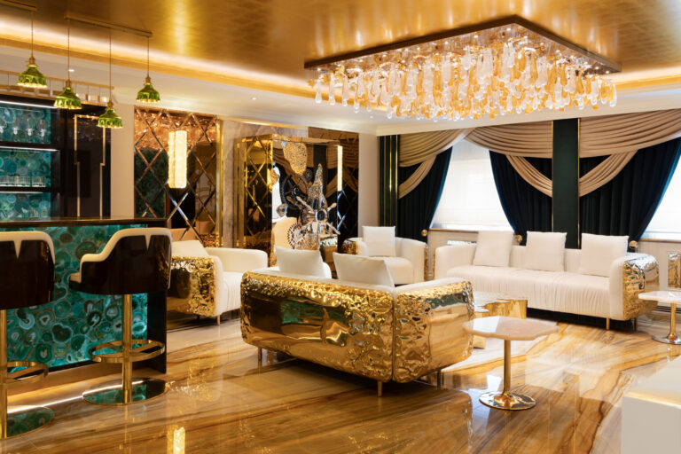 Lounge area with a gilded sofa, white armchairs, a green agate bar front, and a crystal ceiling fixture