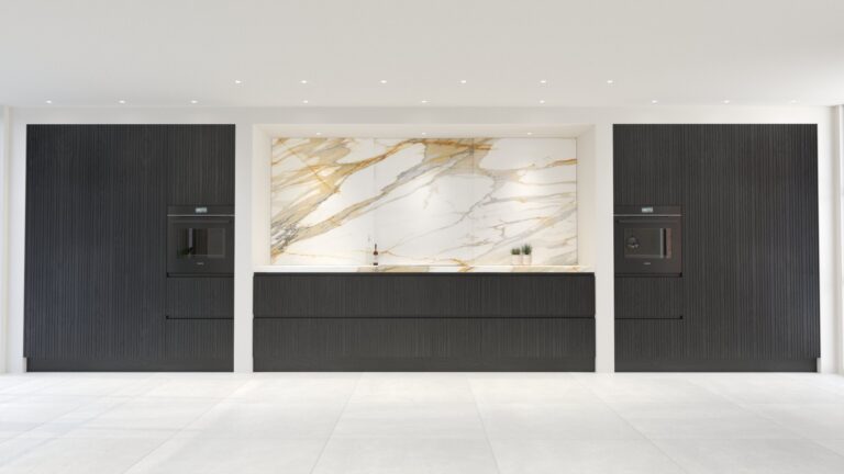 Black timber cabinetry flanks a Calacatta Mediceo stone splashback with integrated ovens and a slim worktop below