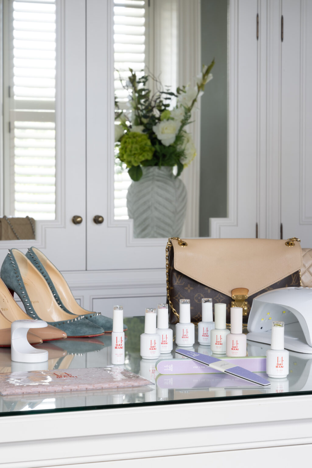 Glass-topped dressing table with heels, a handbag and manicure bottles against panelled wardrobes and shuttered windows