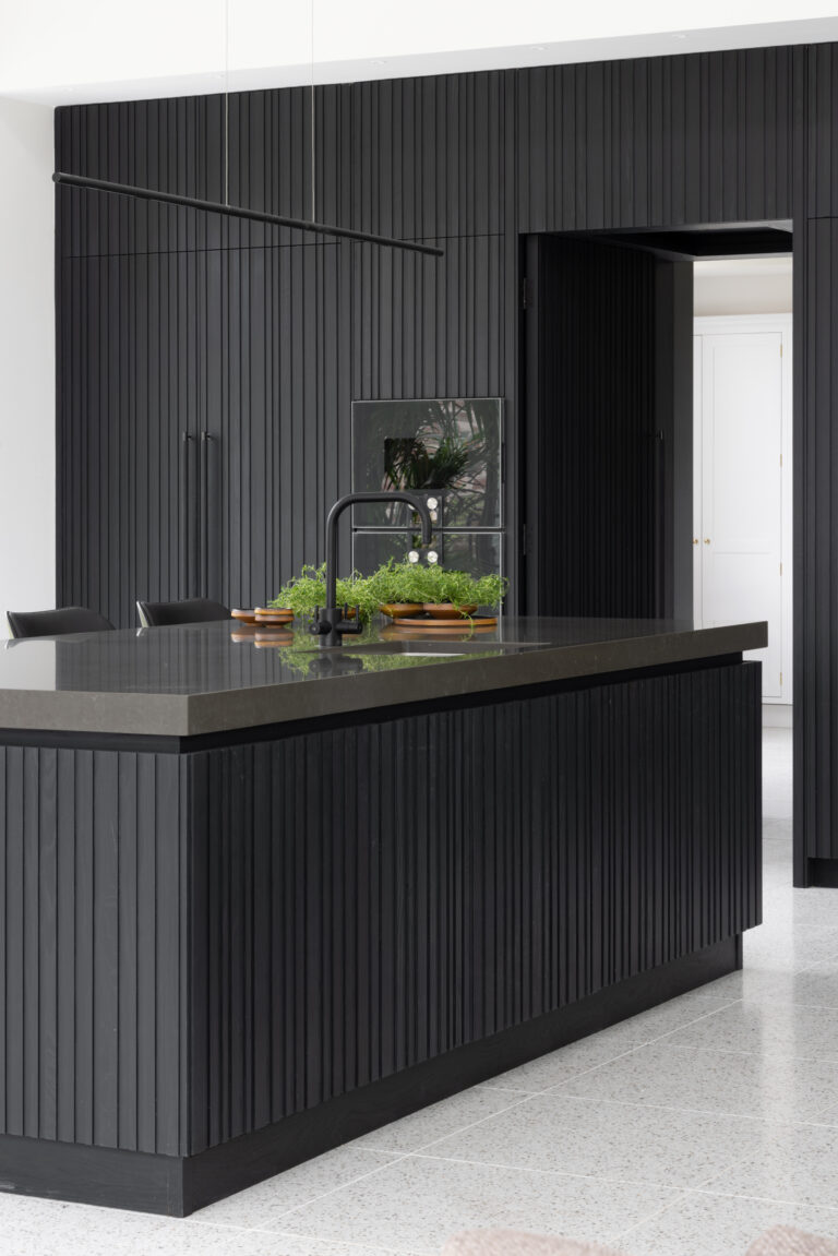 Slatted island with black tap and worktop, dark panelled wall concealing a hidden doorway beyond