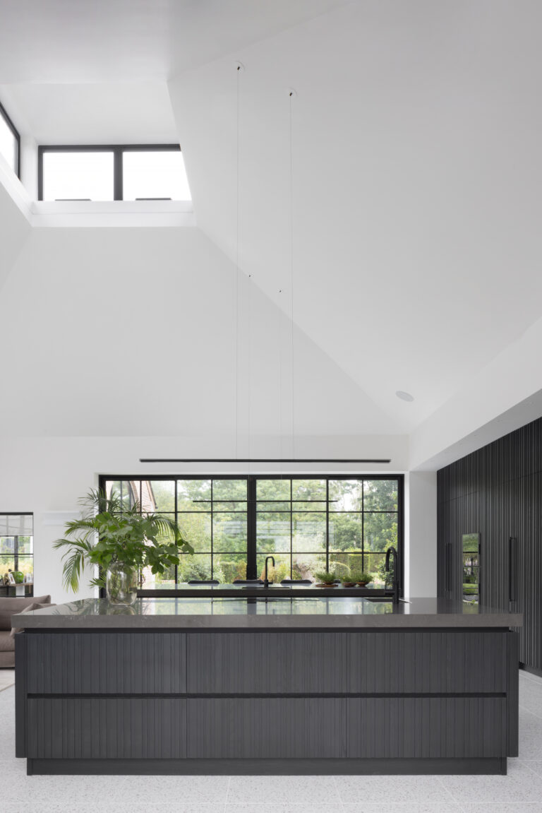 Slatted dark island units beneath tall Crittall glazing, with a vaulted ceiling and garden views beyond