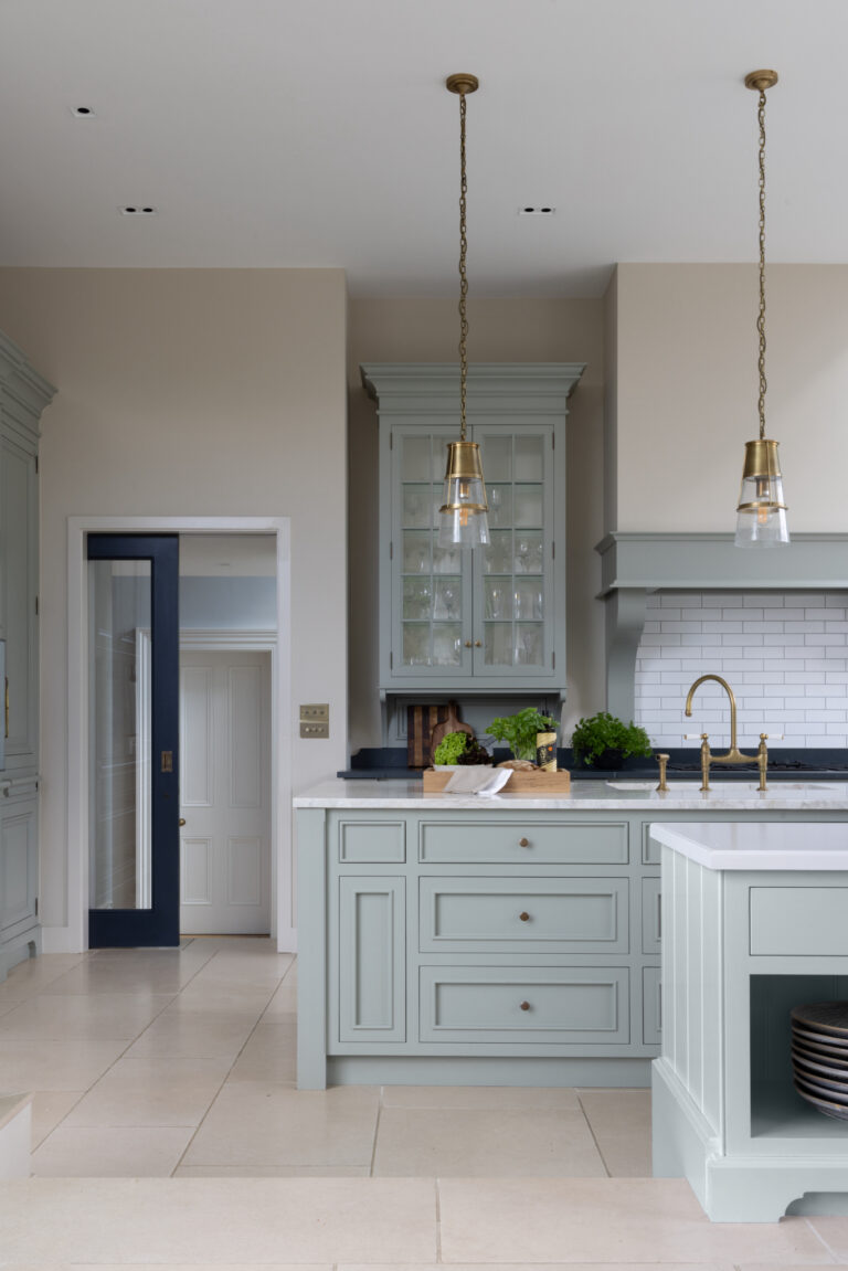 Sage-painted kitchen island with glazed dresser, brass pendant lights and aged brass tap over a marble worktop