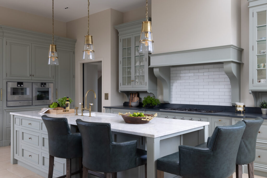 Sage-painted kitchen with marble-topped island, leather bar stools and a corbelled canopy over the hob