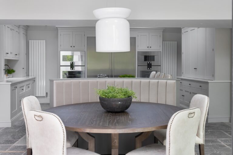 Round dining table with upholstered banquette seating, surrounded by grey cabinetry and integrated appliances