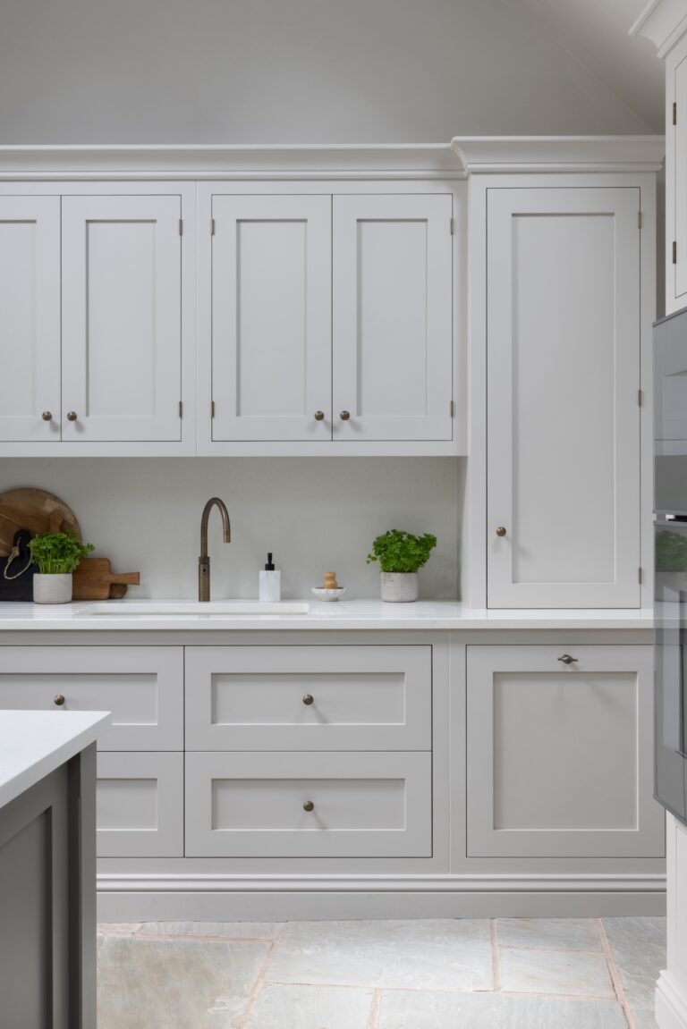 Shaker-style cabinetry with brass knobs, a worktop sink with brass tap, and potted herbs on the counter
