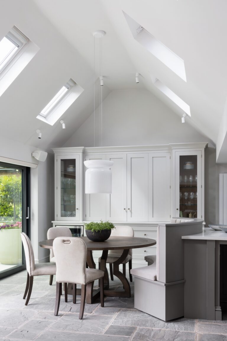 Vaulted ceiling dining area with round table, upholstered chairs and built-in display cabinets beneath rooflights