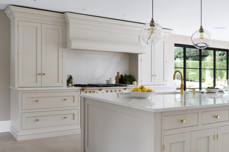 Open-plan kitchen with a Lacanche range beneath a panelled extractor canopy, brass fittings and a large central island