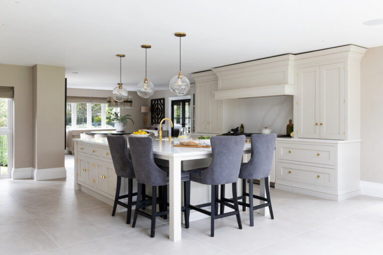 Open-plan kitchen with a large island, grey velvet bar stools, brass fittings and a range cooker beneath an extractor canopy