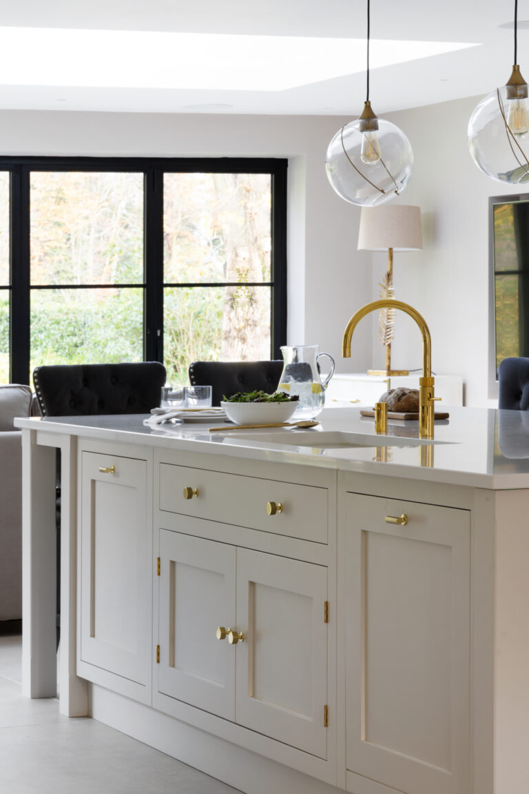 Kitchen island with shaker-style cabinetry, brass handles and tap, and worktop bar seating for dining