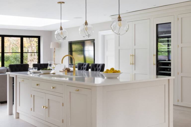Open-plan kitchen island with brass tap and fittings, integrated wine conditioner and glass globe pendant lights above