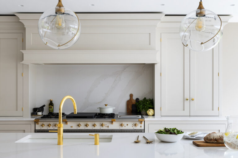 Kitchen with a Lacanche range, brass tap and pendant lights above an island with bread and salad