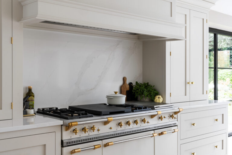Professional Lacanche range with brass fittings set within cabinetry below a stone-effect splashback and extractor canopy
