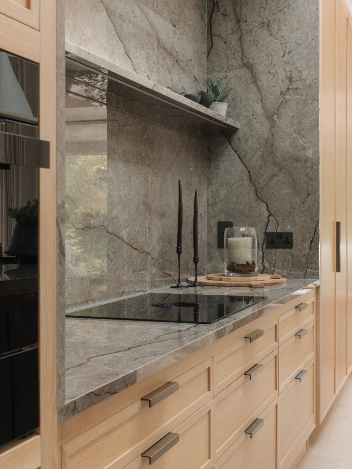 Astana Grey stone splashback and floating stone shelf above a Bora induction hob, framed by Cotton White oak drawers with aged brass bar handles