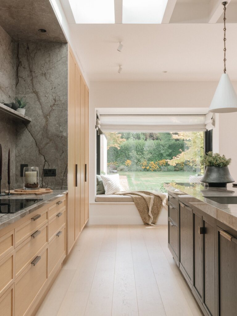 Walkway between Cotton White oak drawers and a black-stained oak island, leading to a window seat overlooking the garden, with an Astana Grey stone wall on the left