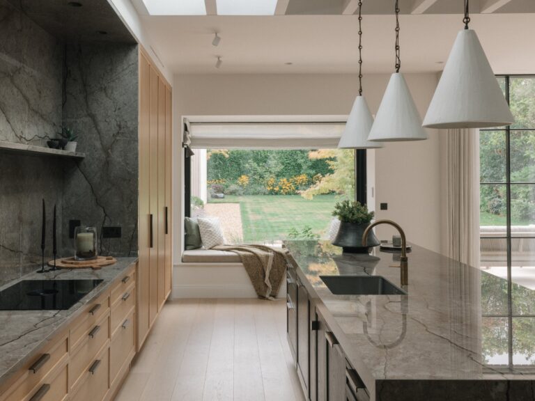 Wilmslow kitchen under rooflights, with Cotton White oak cabinetry and an Astana Grey stone wall on the left, a black-stained oak island on the right and a window seat overlooking the garden